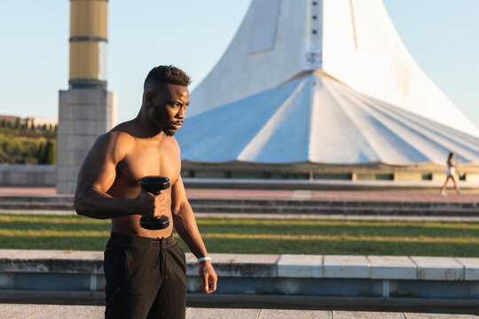 Athlete exercising with dumbbell while standing at park