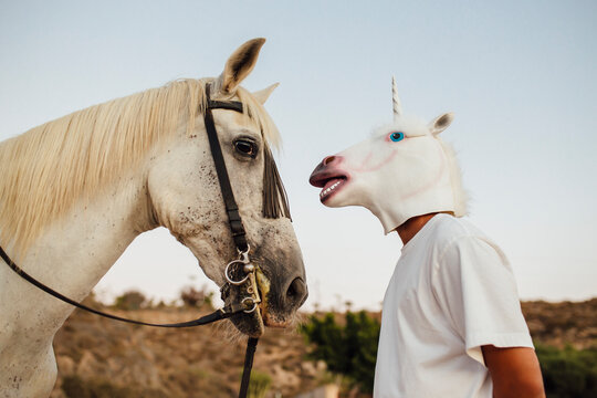 White horse and man wearing unicorn mask looking at each other