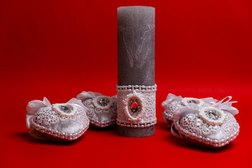 Decorative candle surrounded by four handmade hearts with crystals inside on a red background.