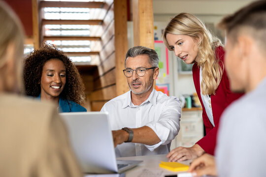 Businessman using laptop while explaining colleagues in meeting at office