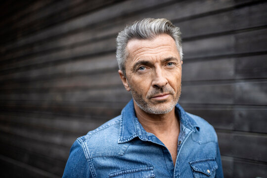 Mature man staring while standing against wooden wall