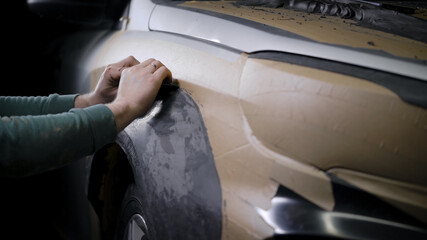 male constructor is producing prototype of detail from modeling clay, covering car body in workshop...