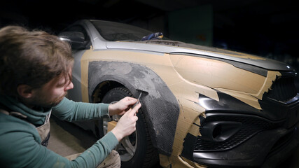 designer man is creating clay form for tuning car body in garage, grinding plasticine, shaping...