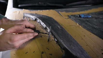 A master with loops in his hands displays the shape of a part. A man works on a mock-up of a sports hood for a car. Tuning atelier