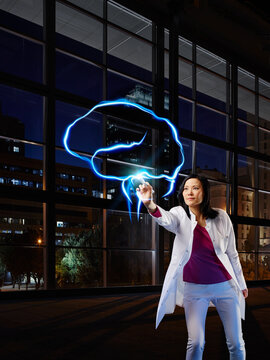 Mature female neurologist analyzing brain with light painting at hospital