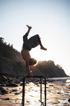 Shirtless young man practicing handstand on parallel bars at beach
