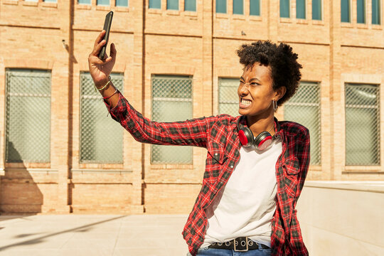 Young woman clenching teeth while taking selfie through mobile phone against building
