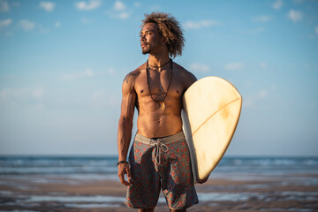Shirtless young man with surfboard looking away while standing at beach against sky