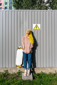 Contemplating young woman with hands in pockets standing against metal wall on sunny day