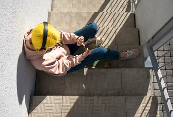 Woman text messaging and listening music while sitting on steps during sunny day