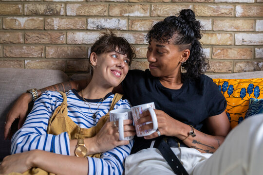 Smiling lesbian couple toasting tea cup while sitting on sofa at home