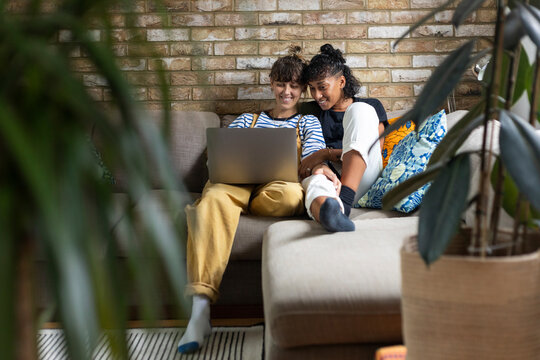 Smiling woman using laptop while sitting by girlfriend at home