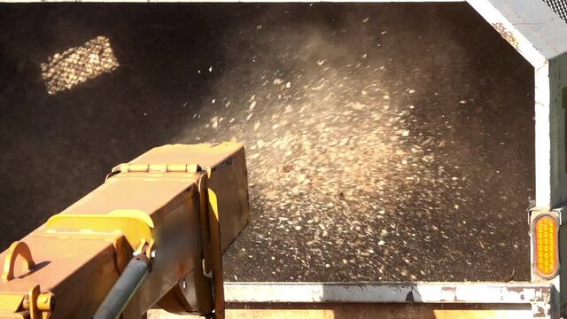 Close-up of wood chips expelled from the chute of wood chipper into the back of a truck in slow motion.