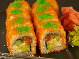 Rolls of fish and cucumber in orange caviar, on a gray plate