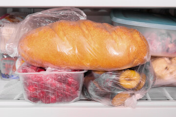 A loaf of wheat bread and other frozen food on a shelf of a home freezer, big procurement and food storage in reserve