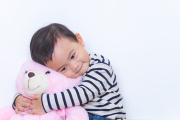 Asian cute baby boy hugging pink bear doll on white background.