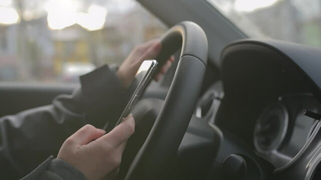 Female driver text messaging on mobile phone on car parking lot, close up selective focus