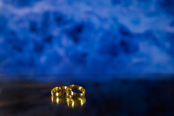 Golden wedding rings on sparkle bokeh background. Selective focus with copy space for text. Wedding card and invitation background. Blue color. 