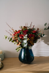 Red bouquet flower arrangement by florist with red roses, poppies and eucalyptus leaves in a blue vase on a wooden table