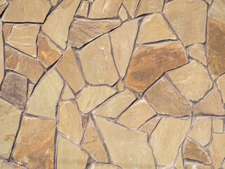 Exterior beige brown wall with decorative masonry made of many pieces of various shapes and sizes