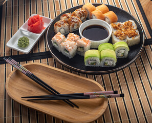 Set of rolls in a Japanese restaurant. rolls on a black plate with wasabi and ginger on a bamboo napkin on the table.
