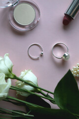 Obraz na płótnie Canvas Silver rings, make up products and white roses on pale pink background. Flat lay.