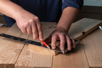 close up of a carpenter working on a wooden board. marking a part with a pencil and a square