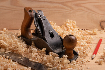 an old carpenter plane, a steel ruler and a pencil on a wooden background with shavings