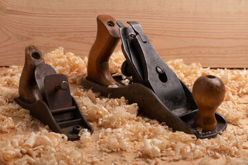 two old carpenter planes of different size on a wooden background with shavings
