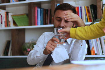 During the quarantine Businessman sits at home using a surgical mask and taking a glass of water.