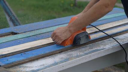 The hands of a worker with a tool on wood. Electro shirt and old boards