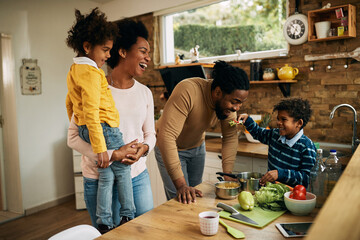 Cheerful black family having fun with healthy food in the kitchen.