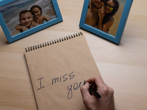 Man's  hand writing words I miss you in the notebook,  photoframes with happy travelling young couple 