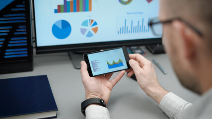 The trader works with electronic reports on the rates of crypto currencies. The bitcoin course is changing rapidly, and you can make good money on this. A man in a shirt in his workplace.