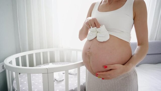 YounYoung pregnant woman with small baby shoes sitting on sofa at home. Expectant mother is preparing for childbirth. High quality 4k footage