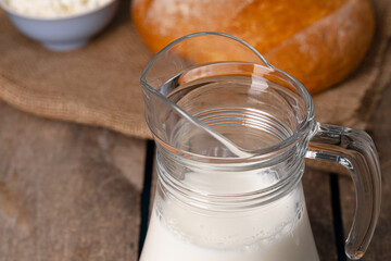 Glass jar of milk, bowl of cottage cheese and bread on wooden table