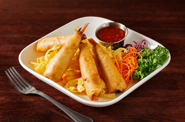 Thai Fried Shrimp Rolls Served with Salad and Chili Dipping Sauce in a white plate on a dark wooden surface