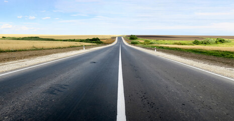 New asphalt road surface on the background of green and yellow fields to the horizon. The construction site for the road works. Highway on the background of a rural landscape        