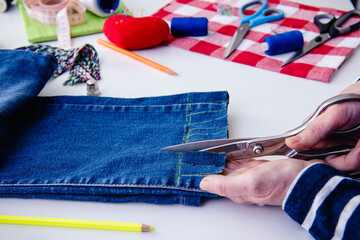 Manos de costurera con tijeras, cortando tiras de la parte inferior de los jeans