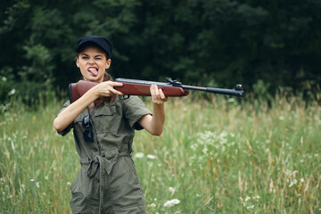 Military woman Shows his tongue with a weapon in his hands in a green jumpsuit black cap 