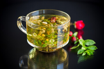 hot herbal tea from various herbs in glass cup on black background