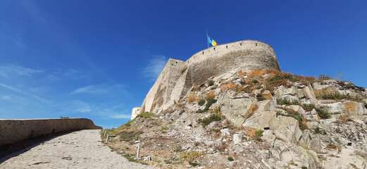 Fototapeta premium The landscape of an old fortress built of stone on top of a rocky hill in Deva, Romania. The flag of Romania flutters in the wind.