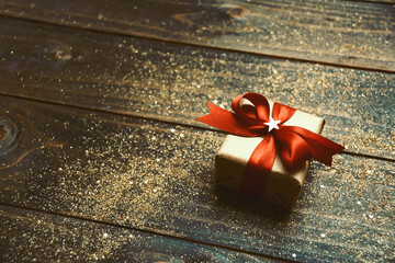 Christmas background - gift box with red bow on wooden board with festive golden glitter 