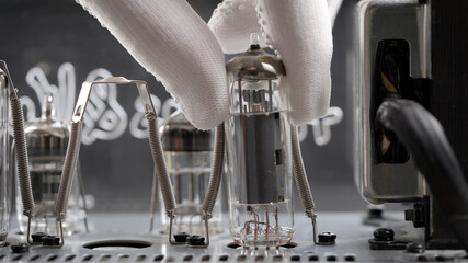 An engineer in a repair shop is replacing old radio tubes. The hand removes the vacuum tube from the amplifier board.