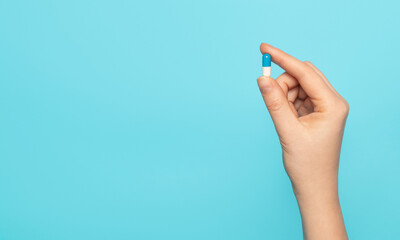 Tablet capsule in hand on a blue background, top view.