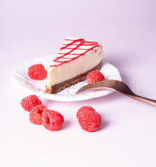 Cheesecake with red raspberries on pink backdrop with fork