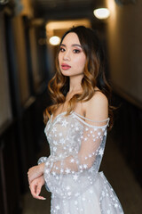 Fototapeta premium Gorgeous young asian woman in elegant dress looking at camera and window, morning of bride, wedding