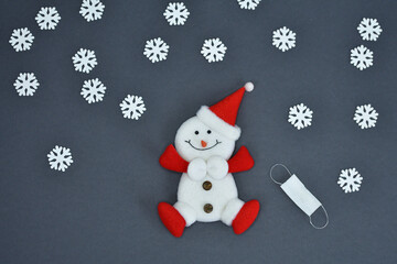 Snowman figurine and medical masks on a grey background. Spruce twigs. New Year, Christmas card.
