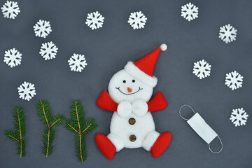 Snowman figurine and medical masks on a grey background. Spruce twigs. New Year, Christmas card.