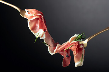Sliced prosciutto with rosemary on forks.